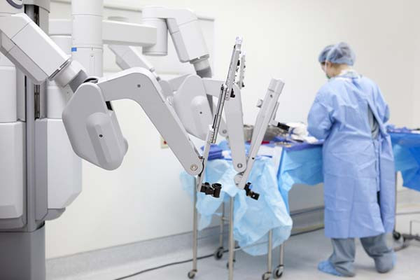 photo of robotic arms used for minimally invasive surgery, with a medical professional in the background, with their back to the camera and slightly out of focus